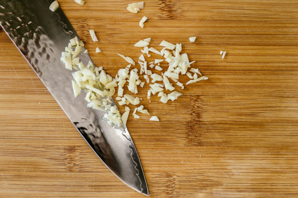 Close-up of chopped garlic on a wooden cutting board with a stainless steel knife.