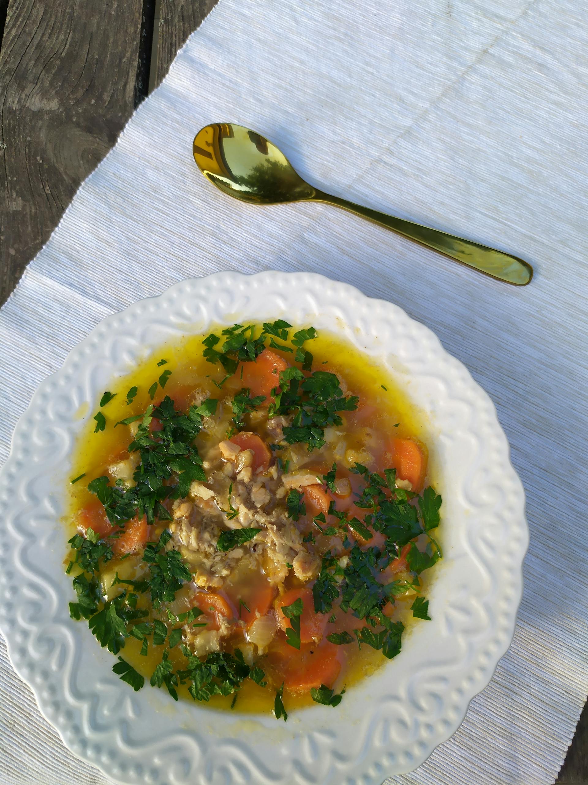 Delicious chicken soup with carrots, parsley, and herbs in a white bowl.