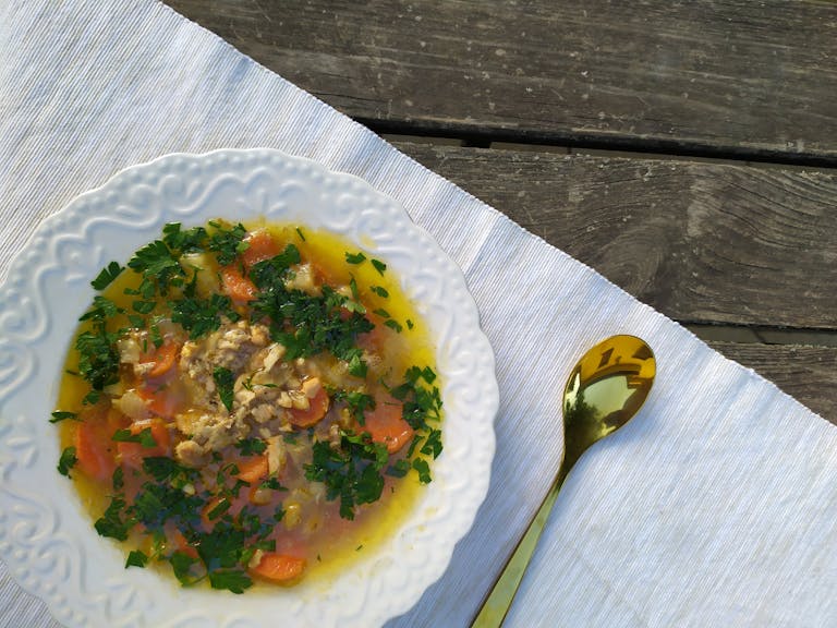 Delicious homemade chicken soup garnished with fresh parsley, served on a rustic table setting.