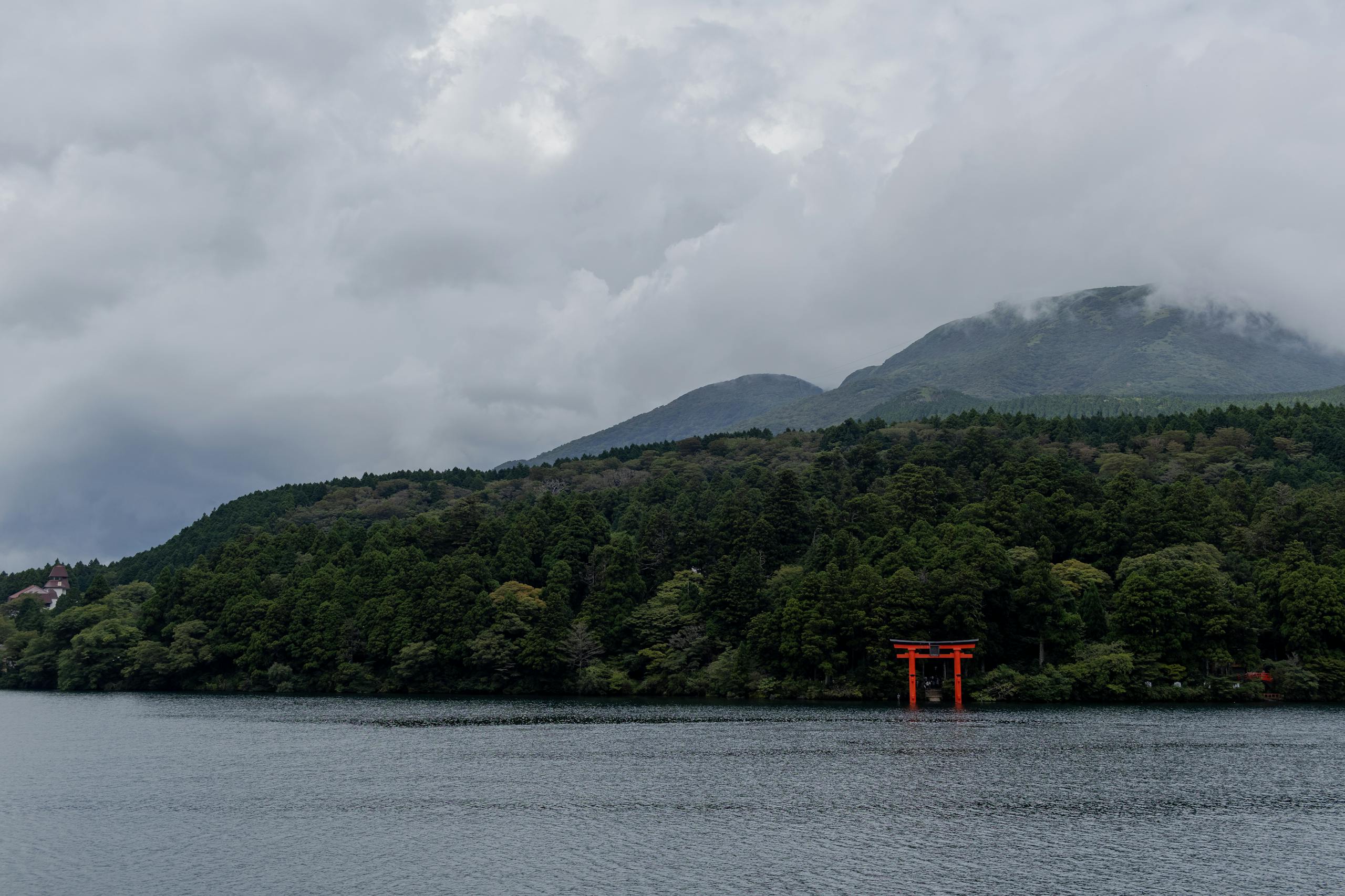 Peaceful scene of Lake Ashi with a vibrant red torii gate and misty mountains.