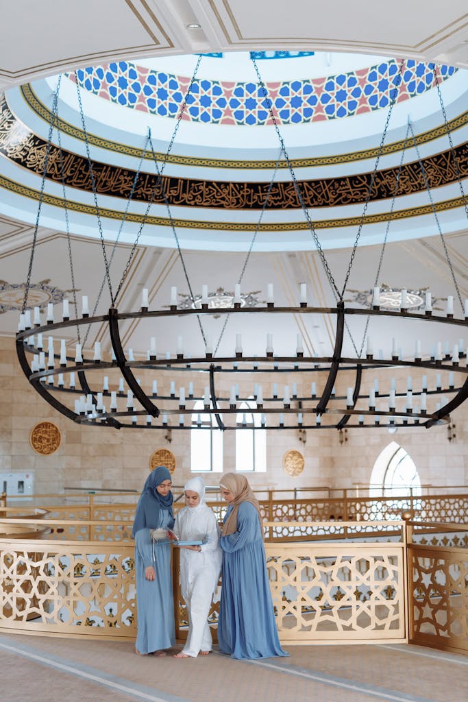 Three Muslim women in traditional attire read the Quran inside a grand mosque, emphasizing faith and togetherness.