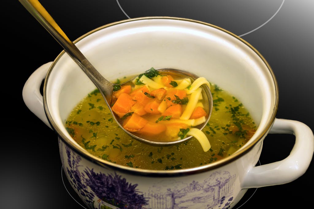 Warm chicken noodle soup with vegetables served in a decorative ceramic pot, perfect for a cozy winter meal.