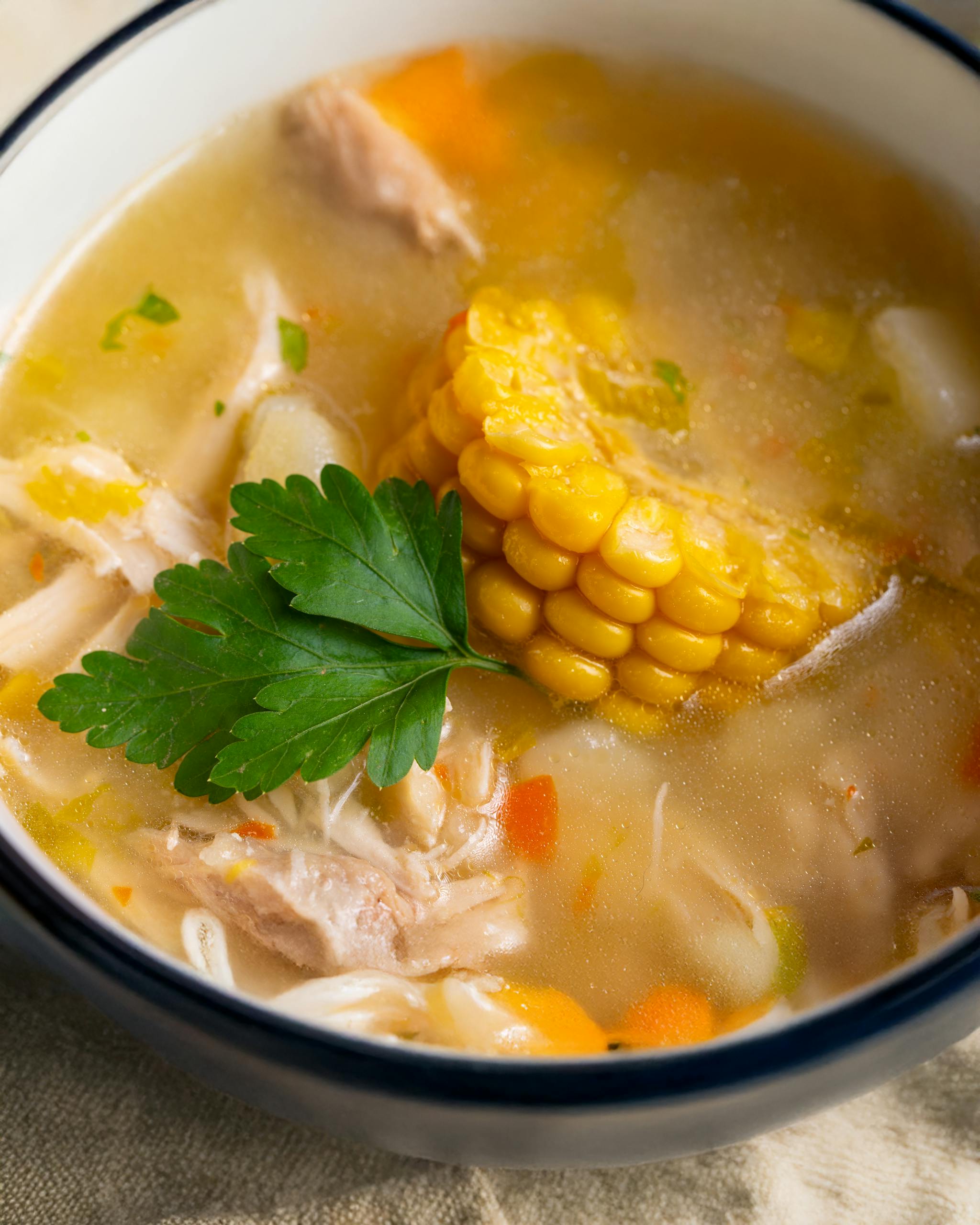 Warm chicken soup with corn, carrot, and parsley, perfect for comforting meals.