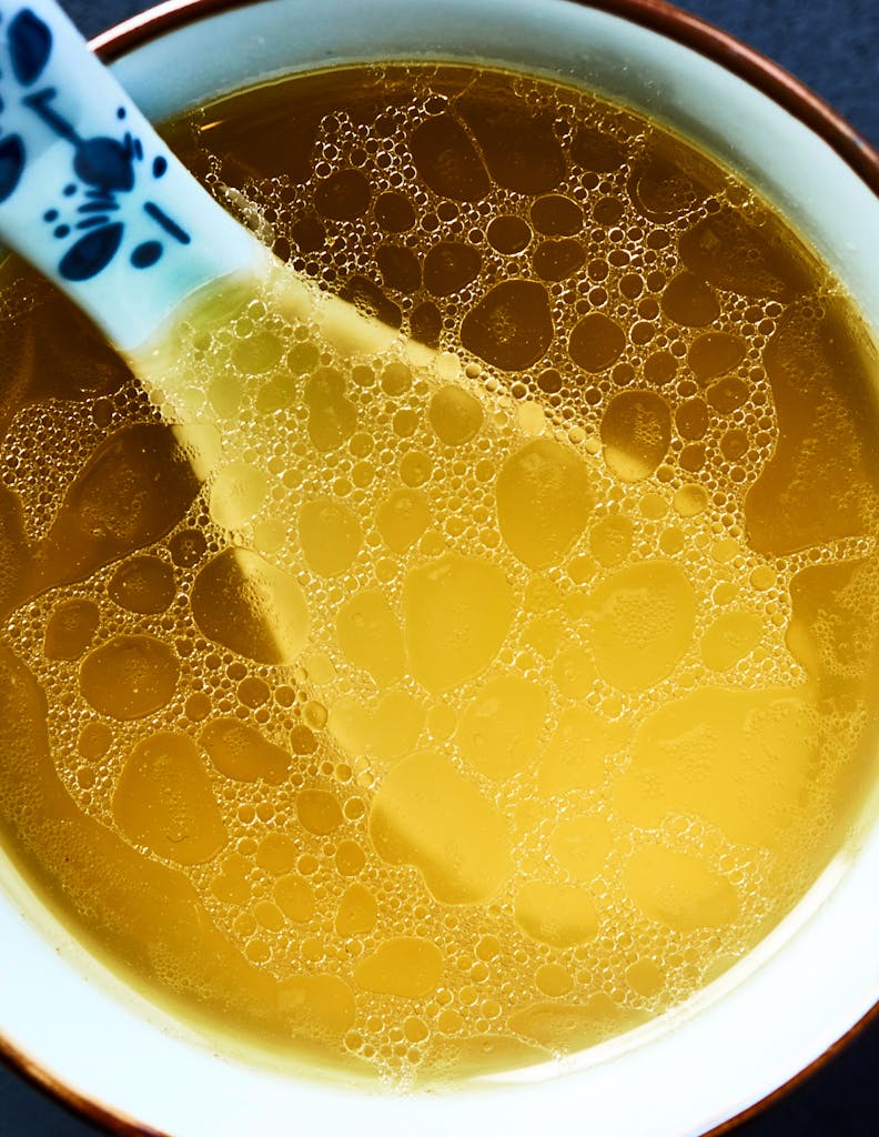 Warm, comforting chicken broth in a bowl with decorative spoon close-up.