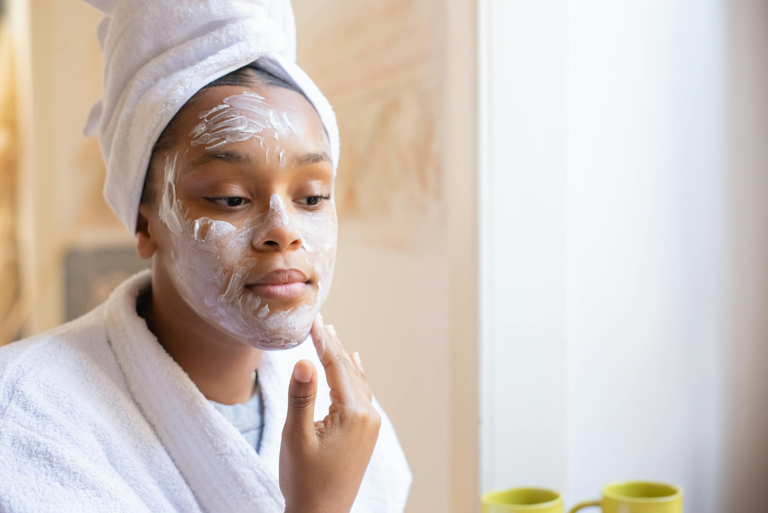 Young woman applying face cream during her morning skincare routine indoors.