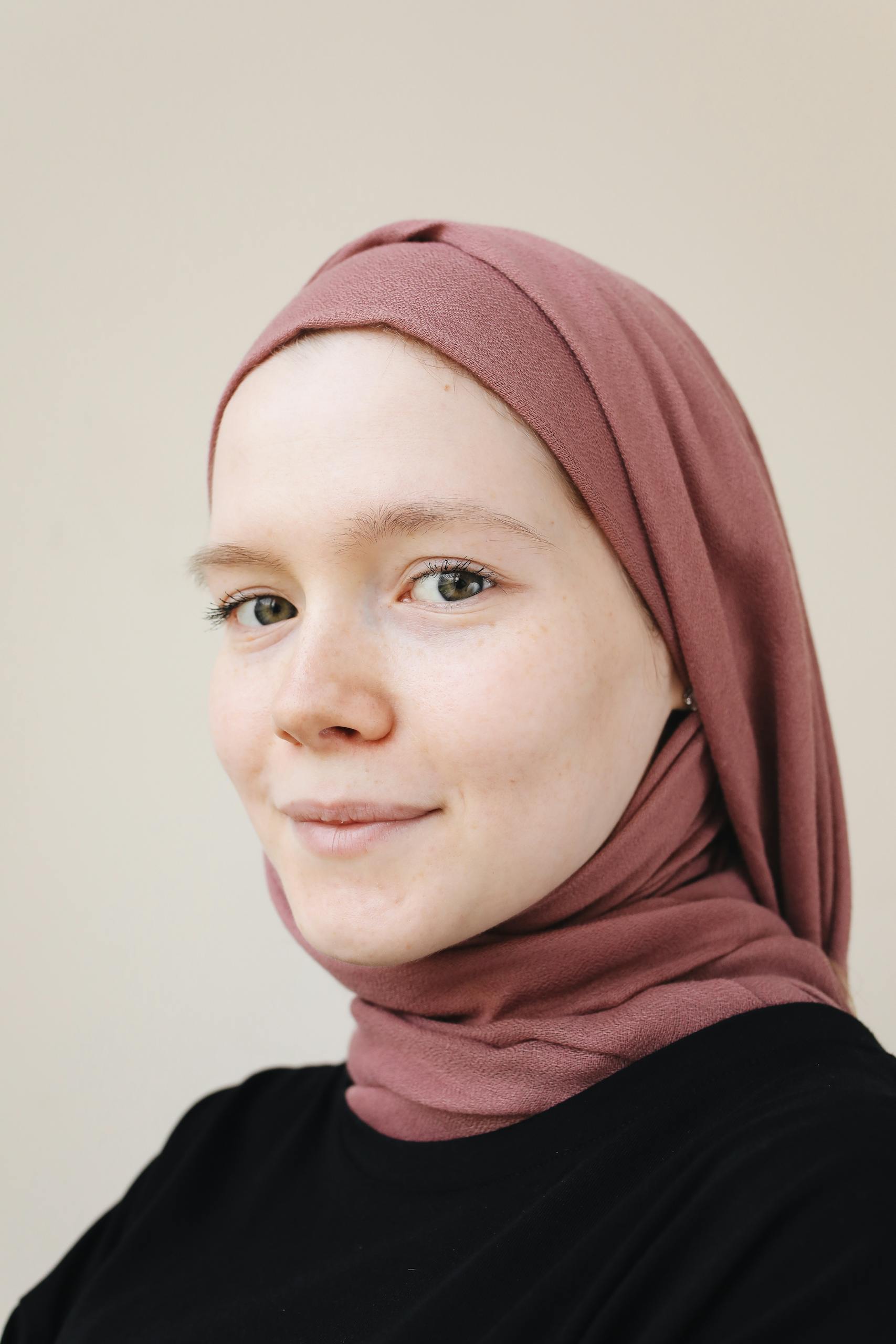 A close-up portrait of a young woman wearing a pink hijab and black top.