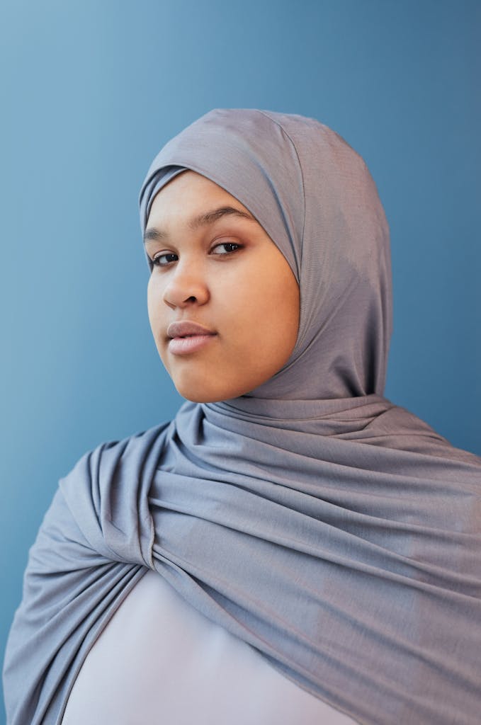 A stylish portrait of a woman in a hijab against a blue background, exuding confidence.