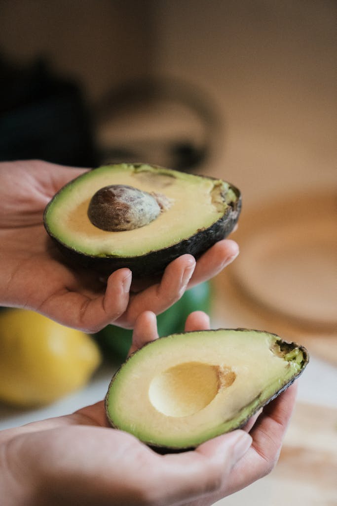 Close-up of hands holding fresh, ripe avocado halves showcasing rich green texture.