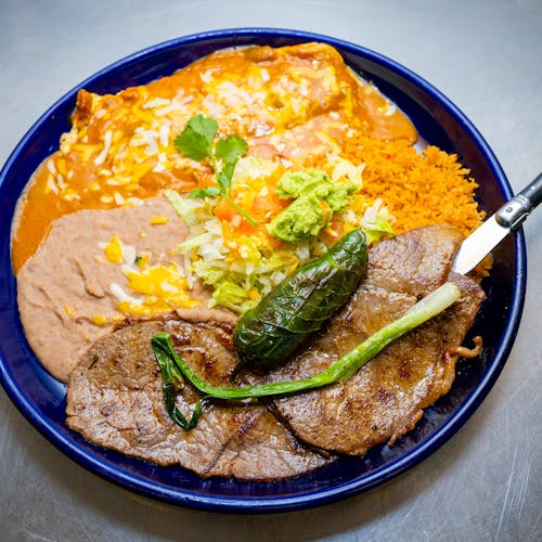 Delicious Mexican dish with steak, enchiladas, and sides on a blue plate.