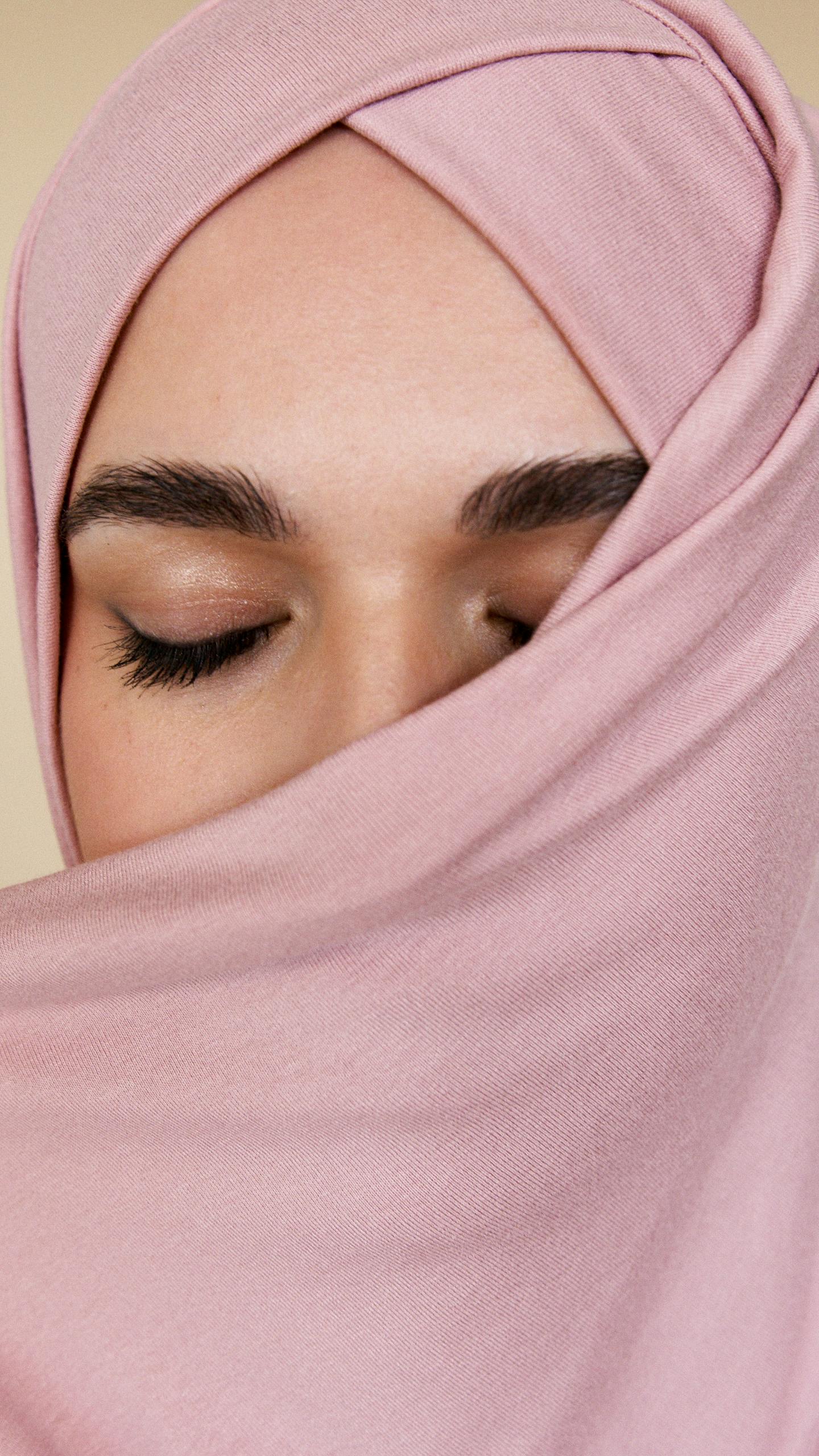 Elegant close-up portrait of a woman with a pink hijab covering her face and eyes closed.