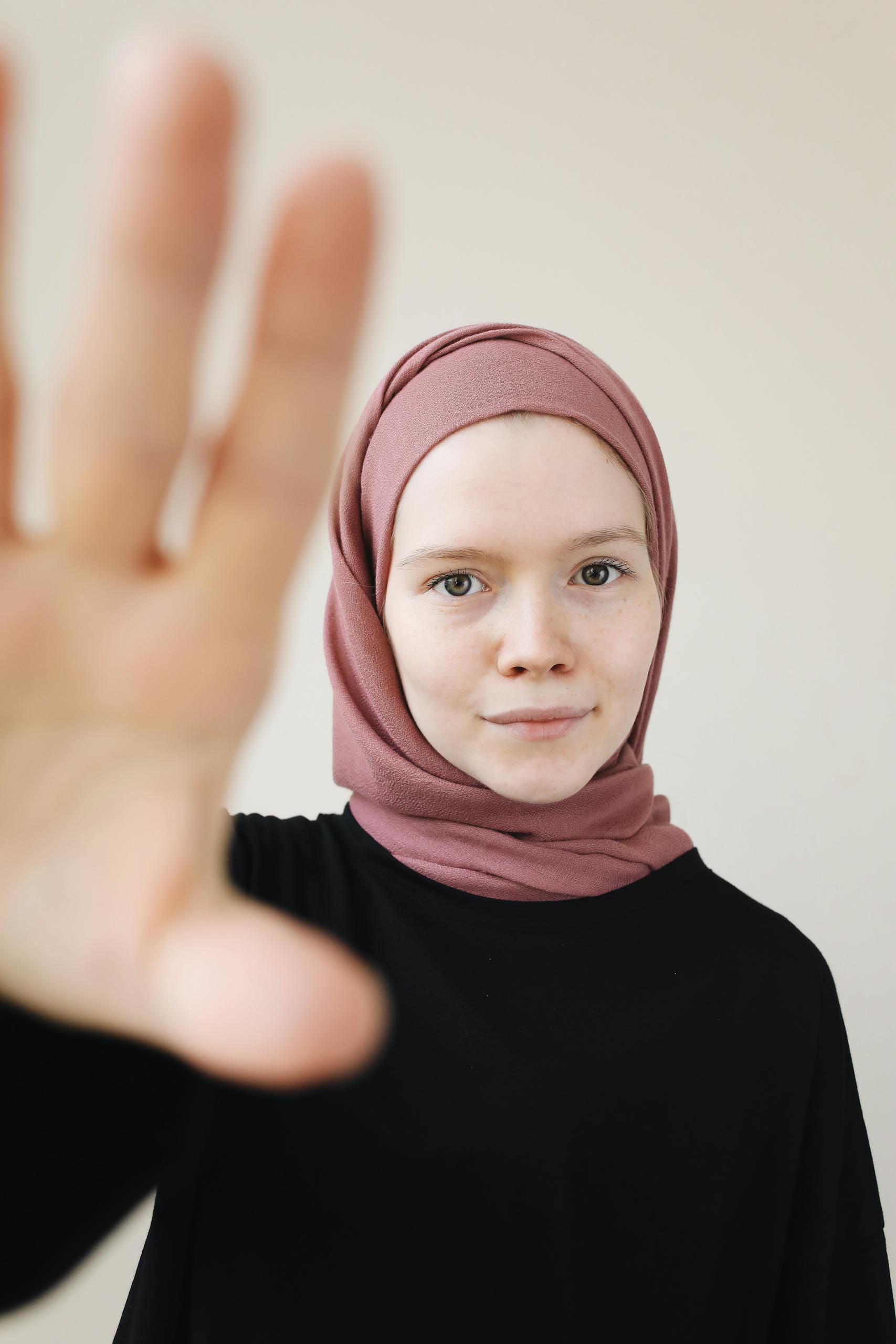 Portrait of a Muslim woman in a hijab reaching towards the camera indoors.