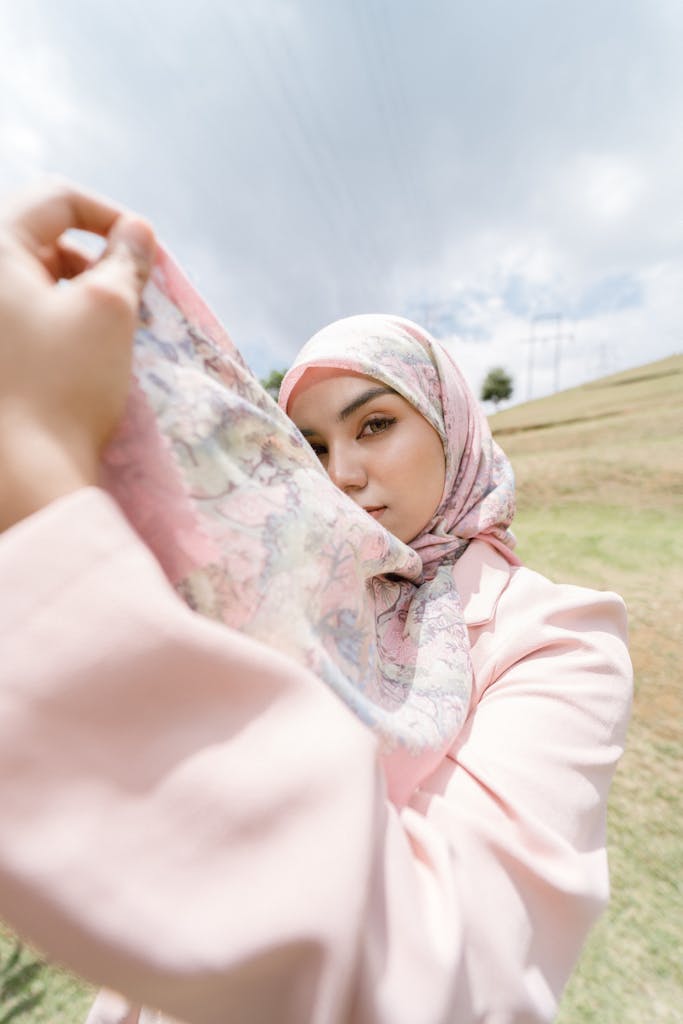 Portrait of a woman wearing a hijab surrounded by outdoor scenery, promoting fashion and elegance.