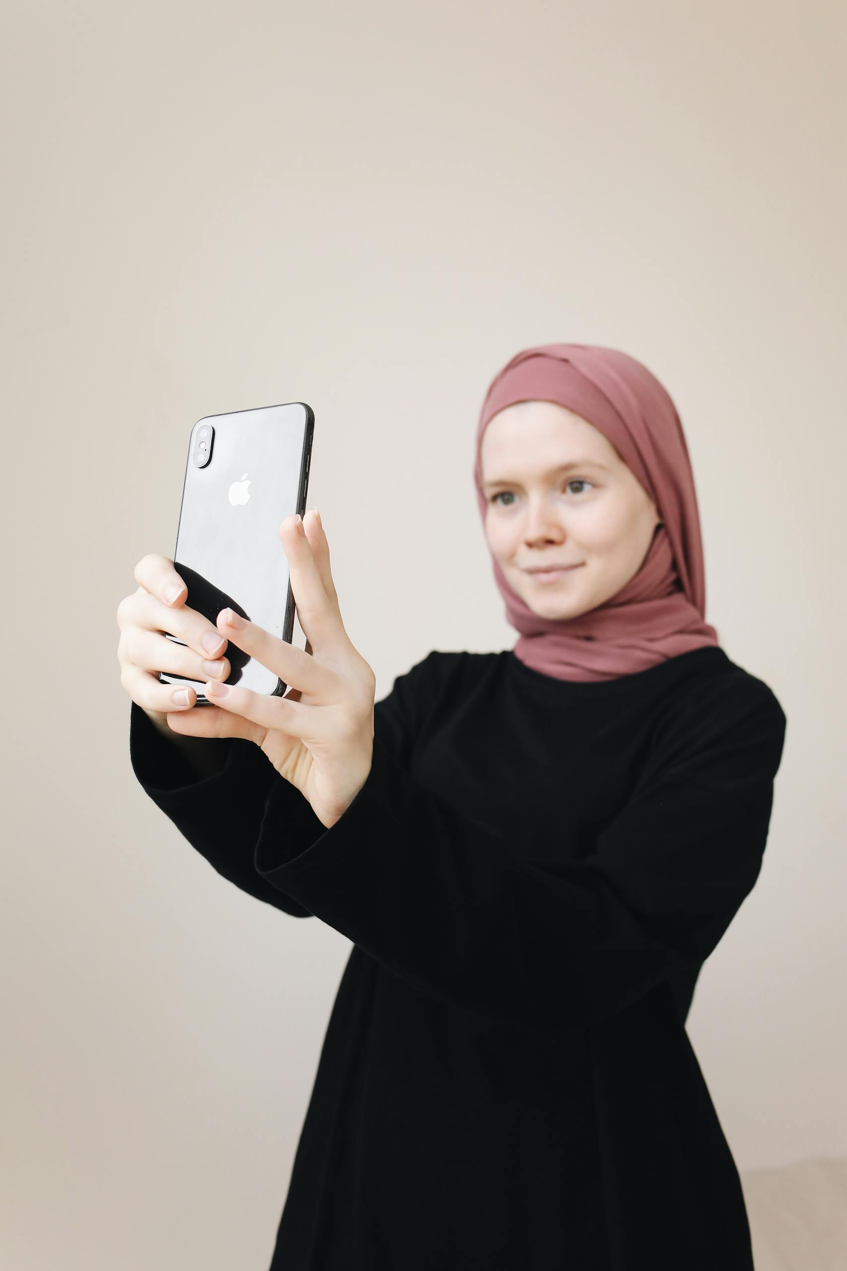 Young woman in hijab taking a selfie with a smartphone indoors.